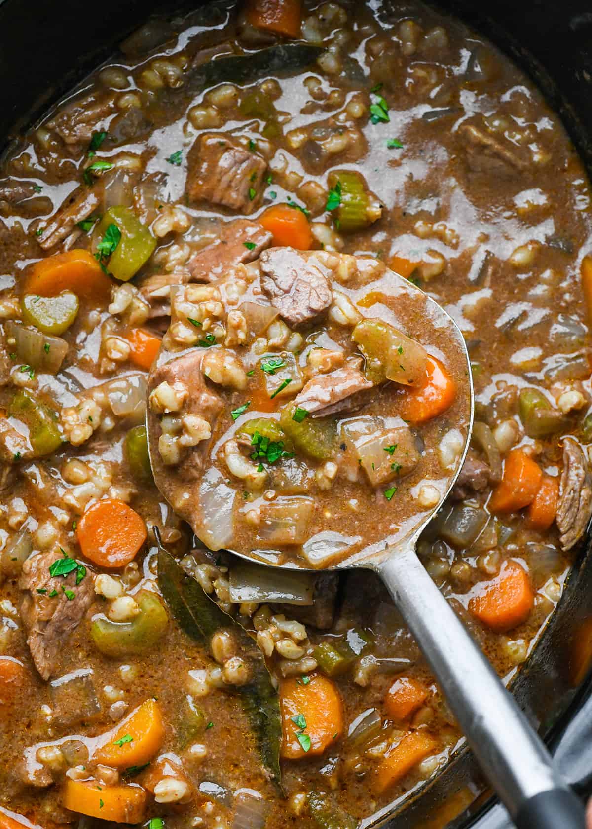 Beef Barley Soup being scooped out of a slow cooker with a spoon