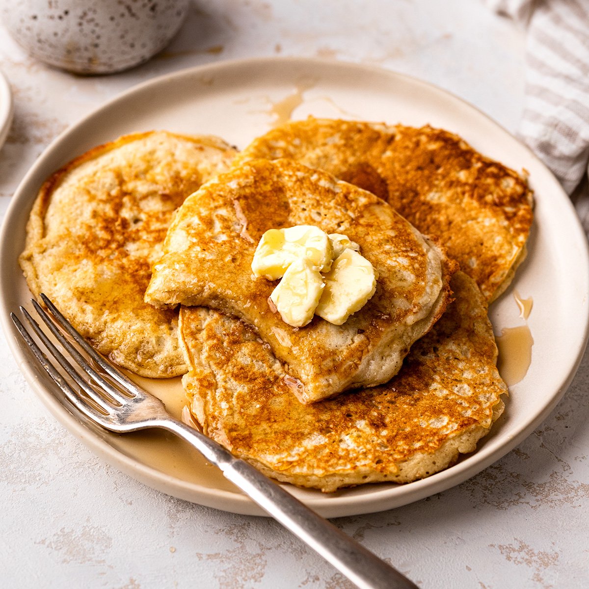 4 Buttermilk Pancakes on a plate with butter, syrup and a fork. 