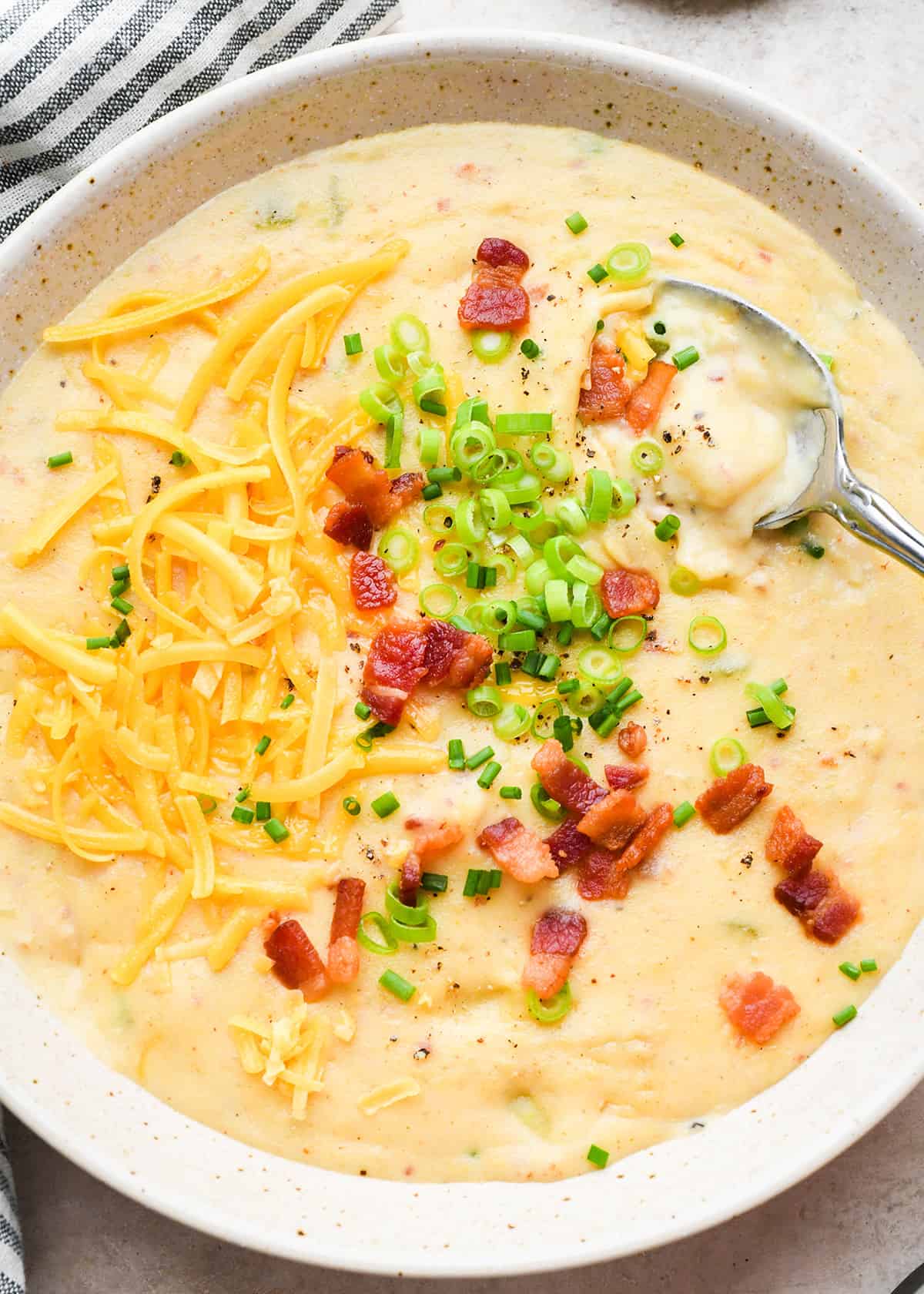 a bowl of potato soup topped with bacon, cheese, green onions and chives. 