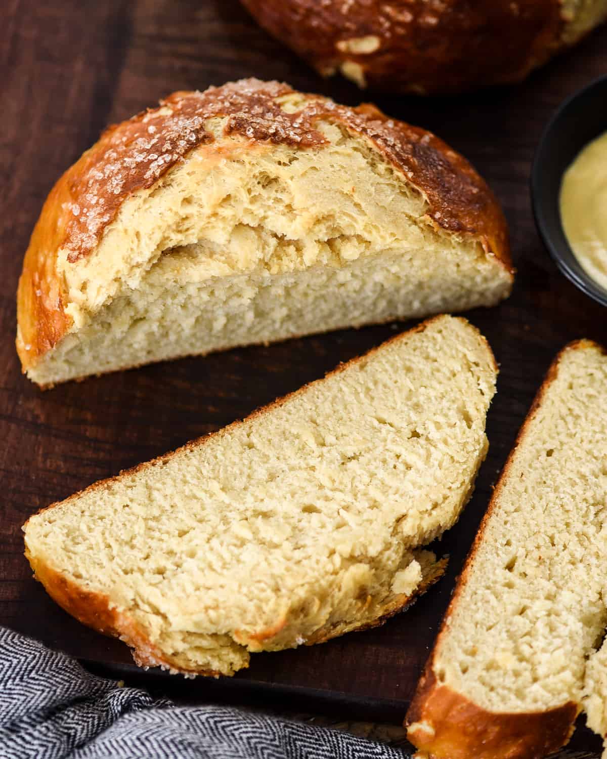 Overhead view of a loaf of homemade pretzel bread on a cutting board with three slices cut and lying down near it