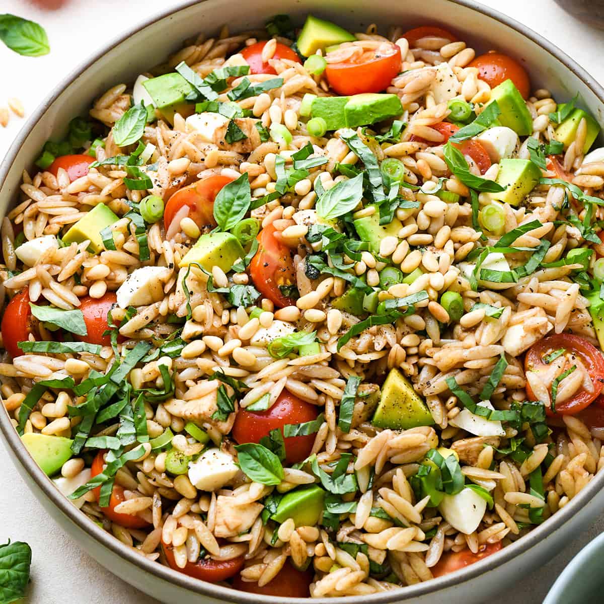 Caprese Orzo Salad in a serving bowl garnished with pine nuts and avocado