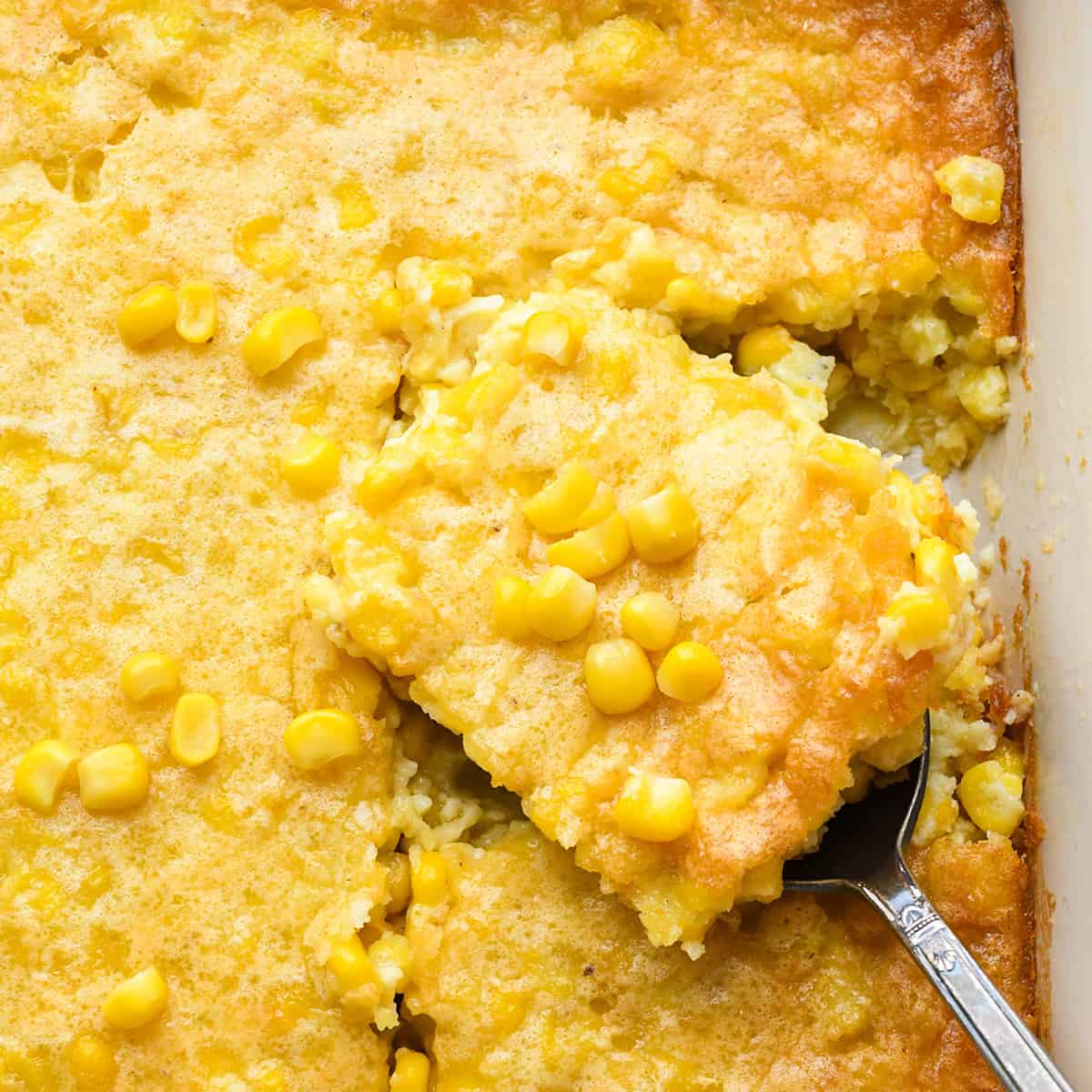 a spoon taking a piece of corn pudding out of a baking dish