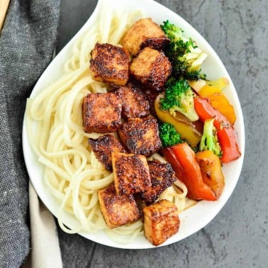 Overhead view of crispy tofu with hoisin sauce on a plate with noodles and stir fried veggies.