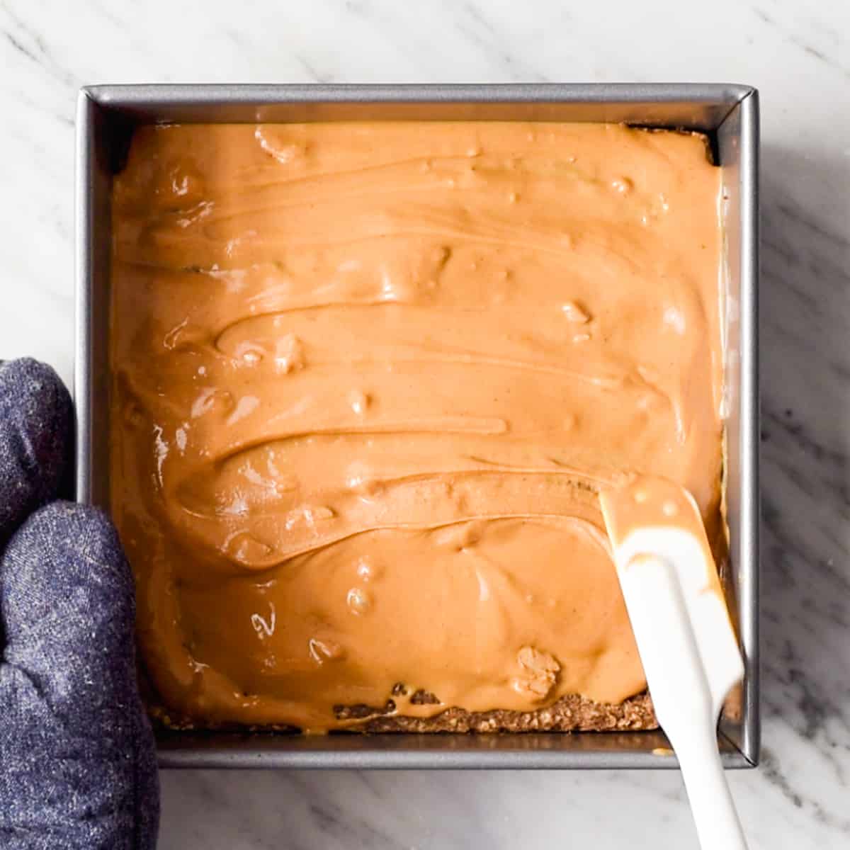 overhead view of hands spreading the peanut butter over partially baked breakfast bars