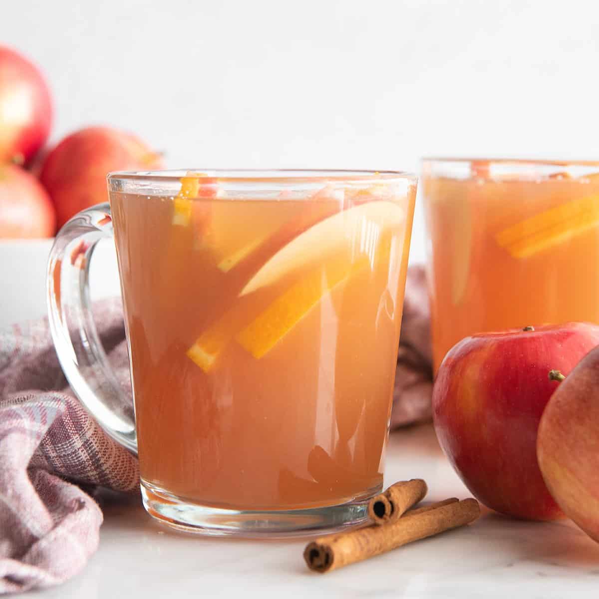 two glass mugs filled with Apple Cider and orange and apple slices