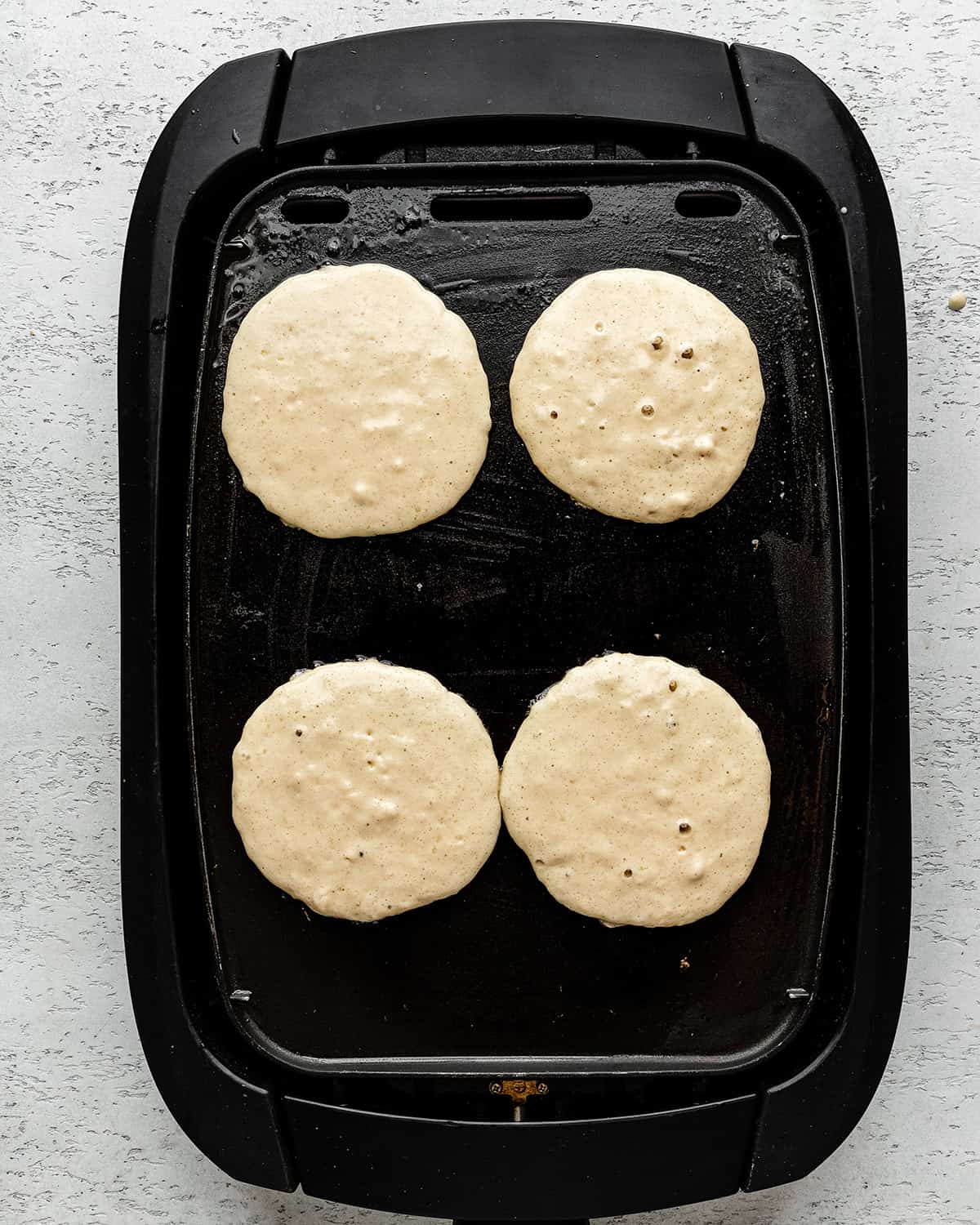 4 buttermilk pancakes cooking on an electric griddle on the first side