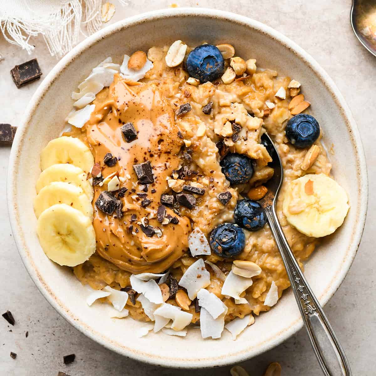 a bowl of Peanut Butter Oatmeal topped with blueberries, bananas, peanut butter, chocolate and coconut