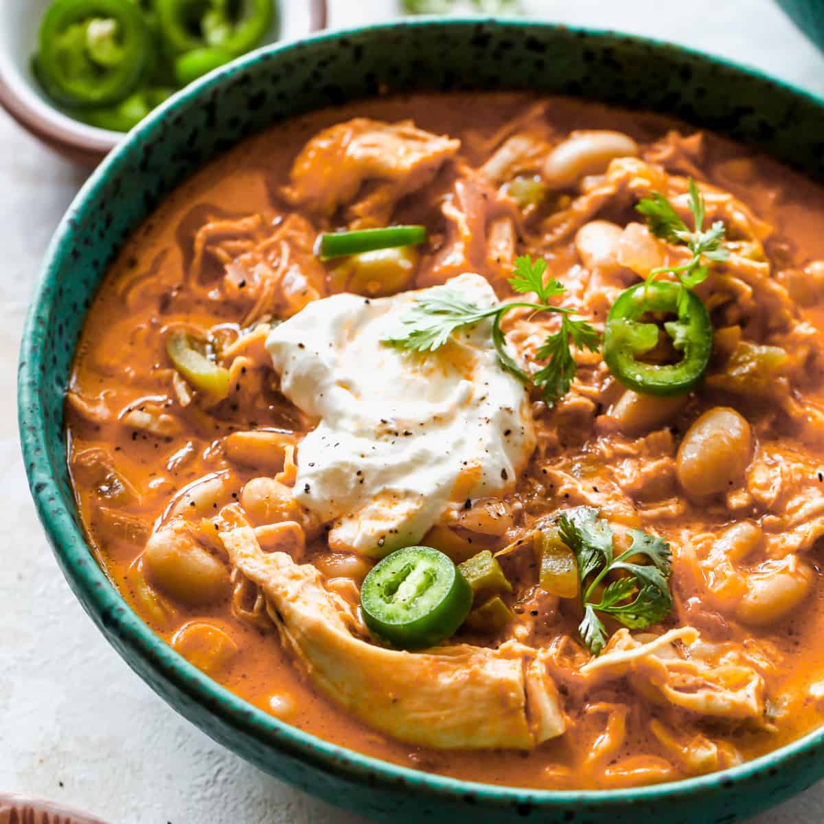 front view of a bowl of White Bean Chicken Chili garnished with sour cream, jalapeños, and cilantro